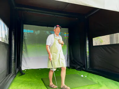 Smiling guest holding a club inside the Golf to Go Events mobile golf simulator at a Sandy, Utah backyard party