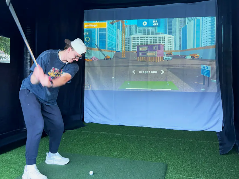 Guest mid-swing with a city skyline on the golf simulator screen at a Salt Lake City party
