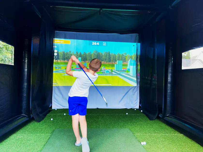 Boy mid-swing on a portable golf simulator minigame at a Utah birthday party