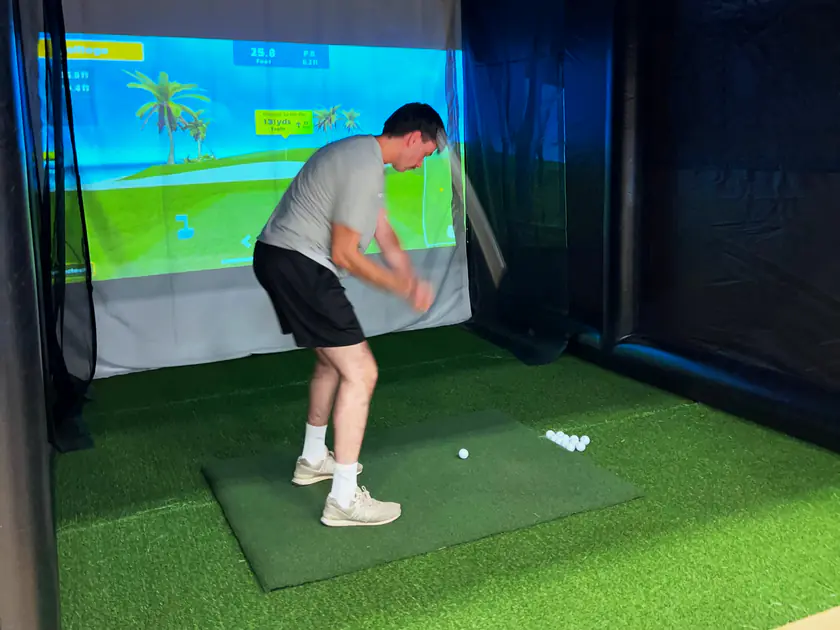 Attendee in casual clothes mid-swing on the Golf to Go Events golf simulator at an indoor trade show