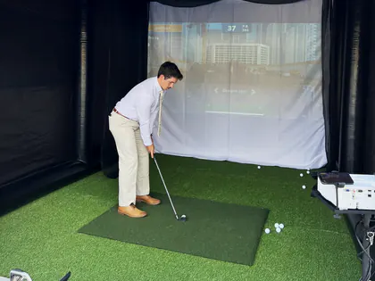 Young guest in dress clothes taking a shot in a mobile golf simulator at a Salt Lake City event