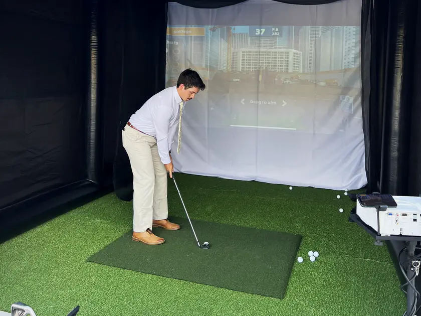 Young guest in dress clothes taking a shot in a mobile golf simulator at a Salt Lake City event
