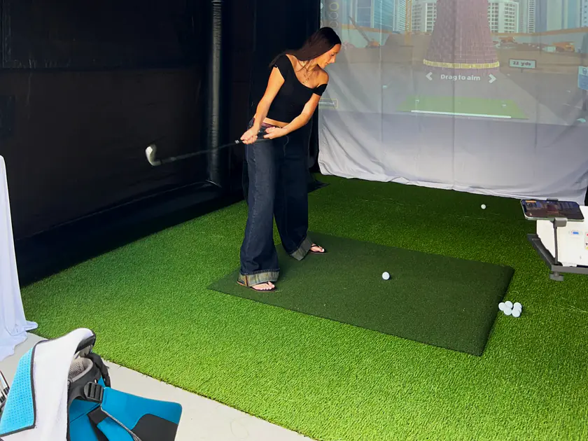 Woman driving off the mat inside a portable golf simulator at an American Fork, Utah event
