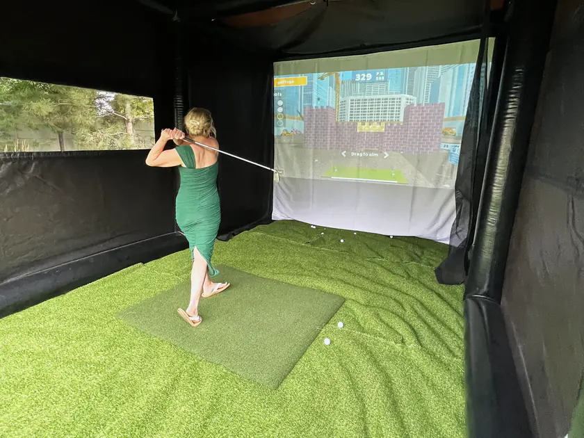 Guest in a green dress swinging inside a mobile golf simulator rental at an Orem party