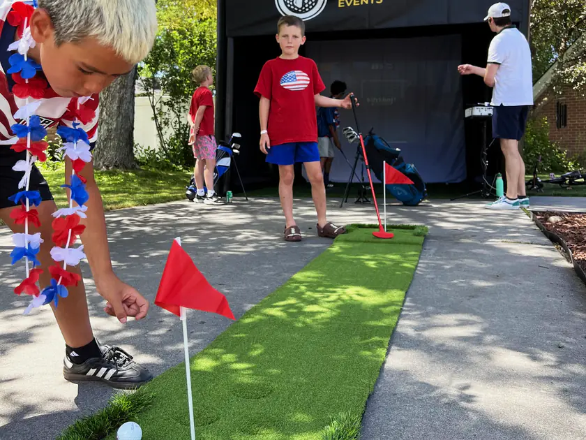Kids in red, white and blue putting beside the Golf to Go Events golf simulator at a Fourth of July community party