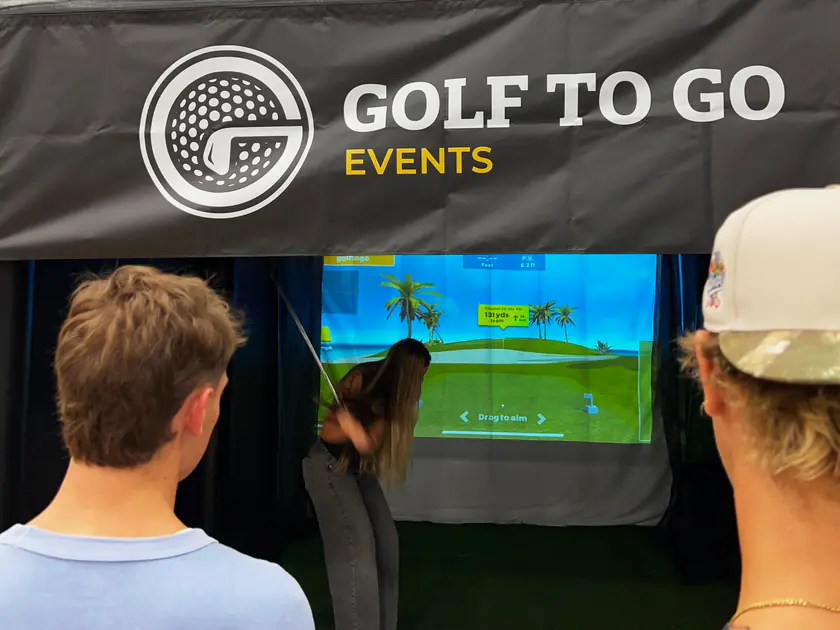 Friends watching a guest take her shot on a mobile golf simulator at a birthday party