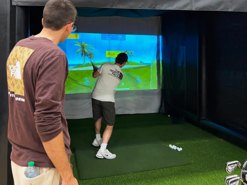 Groomsman watching his friend swing on a portable golf simulator at a bachelor party