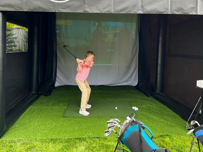 Girl in a pink dress swinging on a portable golf simulator at a West Jordan birthday party