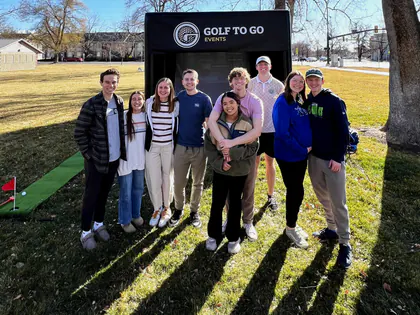 Group of friends posing in front of the Golf to Go Events mobile golf simulator at an outdoor party in Provo, Utah