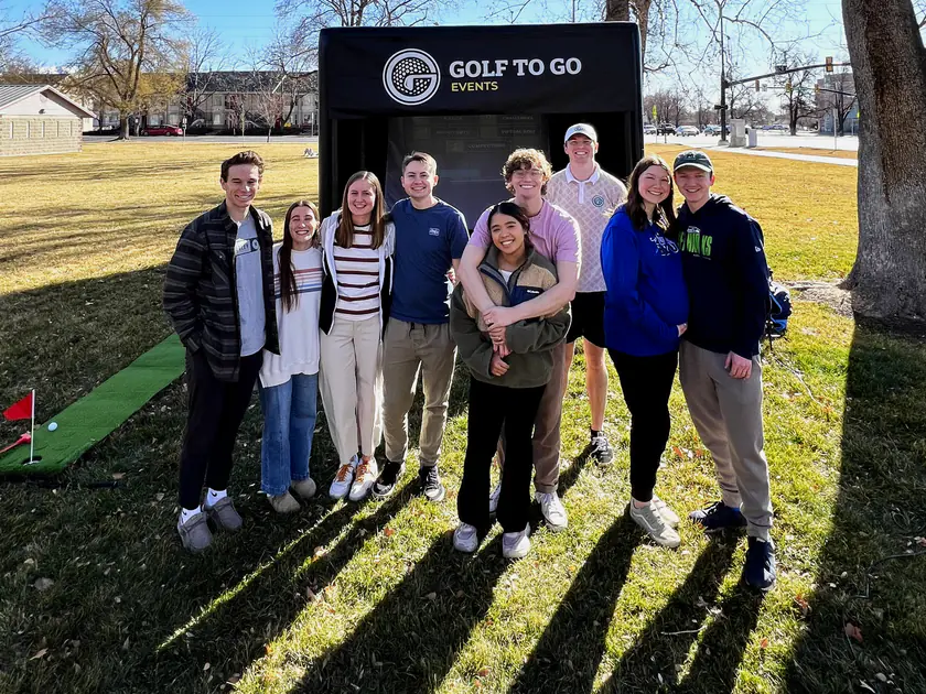 Group of friends posing in front of the Golf to Go Events mobile golf simulator at an outdoor party in Provo, Utah