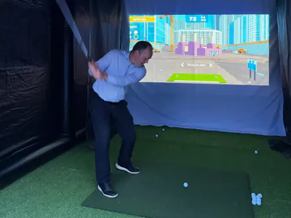 Guest mid-swing on a golf simulator minigame at a Lehi, Utah event