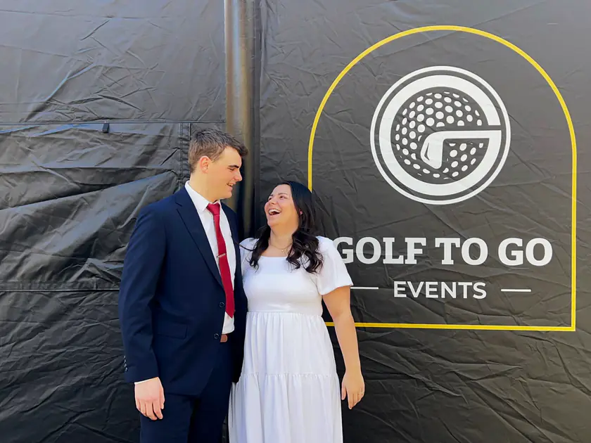 Bride and groom laughing in front of the Golf to Go Events golf simulator tent at their wedding reception