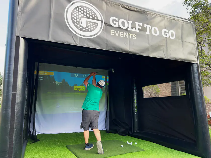 Guest mid-swing inside the branded Golf to Go Events golf simulator tent at a corporate team building event