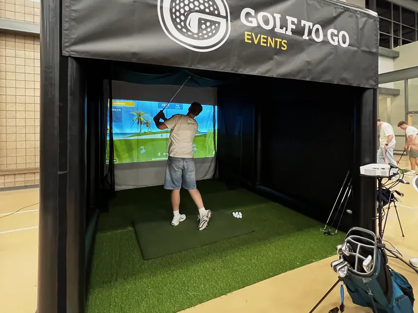 The Golf to Go Events tent on an indoor basketball court at the Provo Rec Center back to school party, a player mid-swing inside