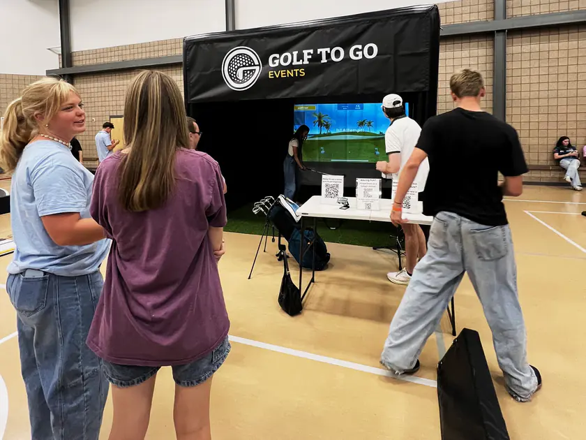 Youth waiting their turn beside a portable golf simulator at an indoor youth activity
