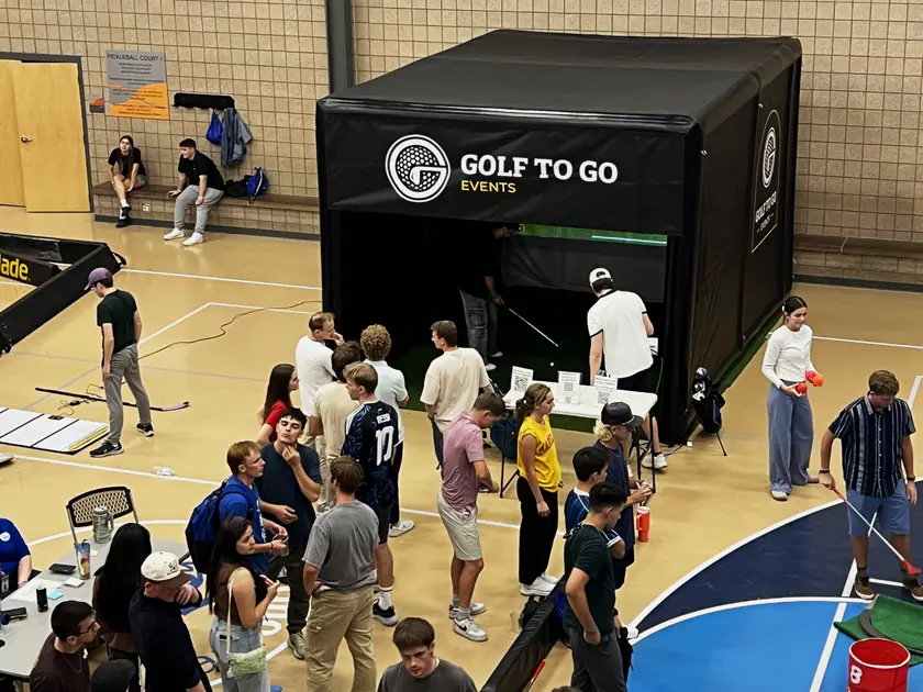 Students crowding a gym around the Golf to Go Events golf simulator at the Provo Rec Center back to school party