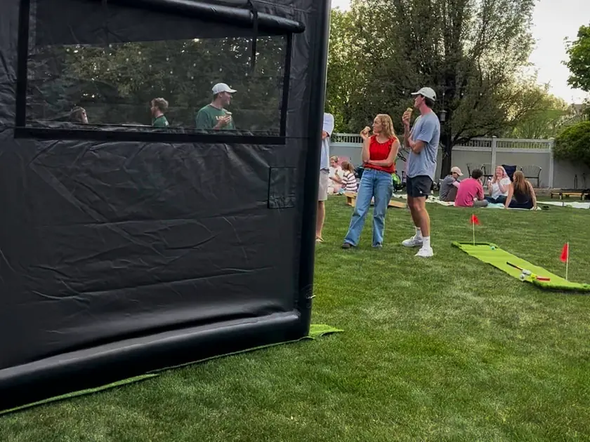 Golf to Go Events simulator tent on a backyard lawn at a group party, guests playing lawn games nearby
