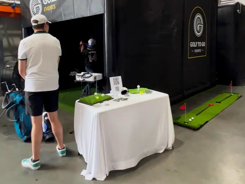 Golf to Go Events golf simulator booth with a welcome table and putting mat at an indoor trade show